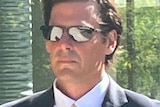 A man in sunglasses and a black suit looks serious.