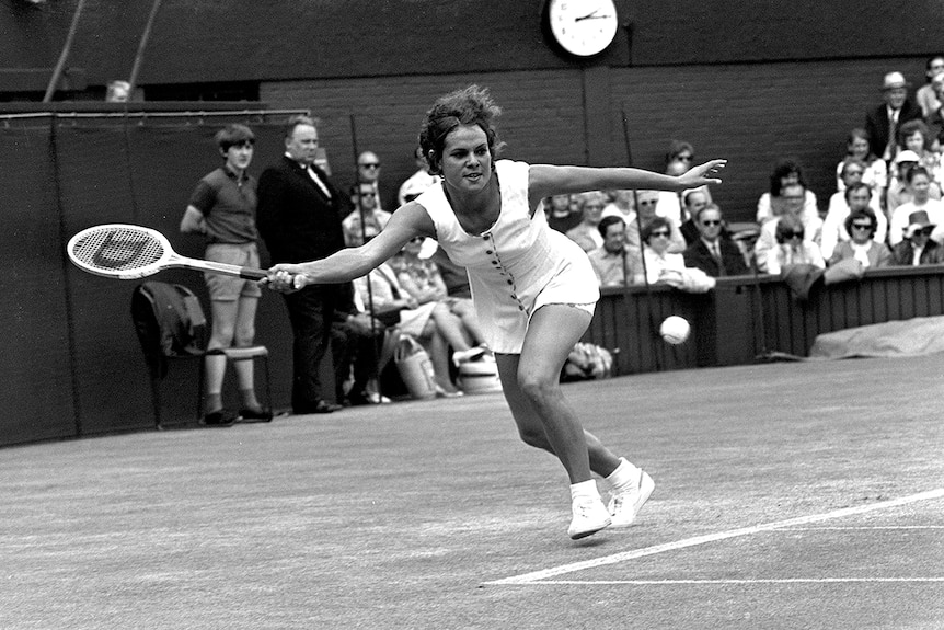 Black and white photo of a woman with outstretch arm reaching to return a shot on grass tennis court at Wimbledon in 1971.