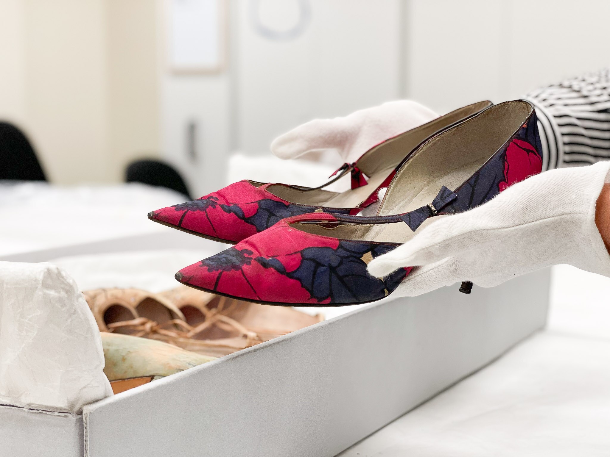 A pair of black and red high-heeled shoes held in gloved hands.