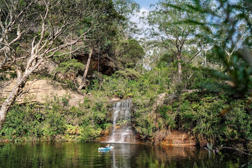 A person floating in Paradise Pool in front of a waterfall