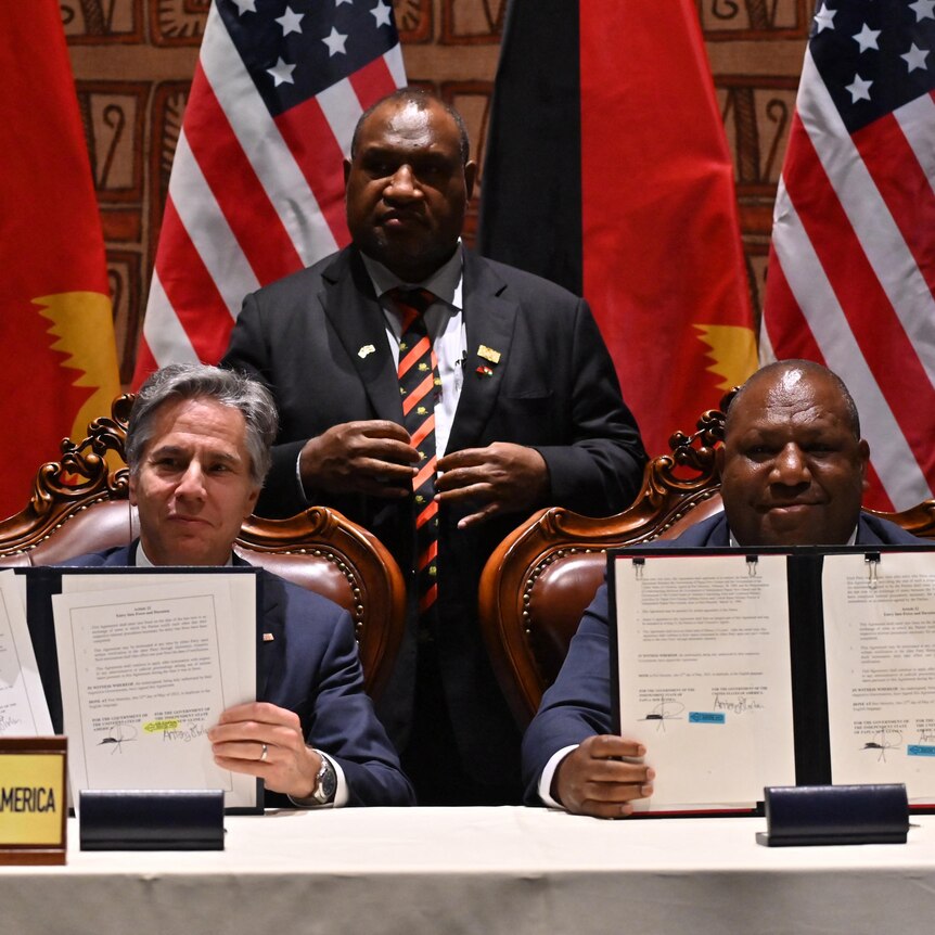 Antony Blinkey and Win Bakri Daki show documents they have just signed while seated at a desk near US and PNG flags.