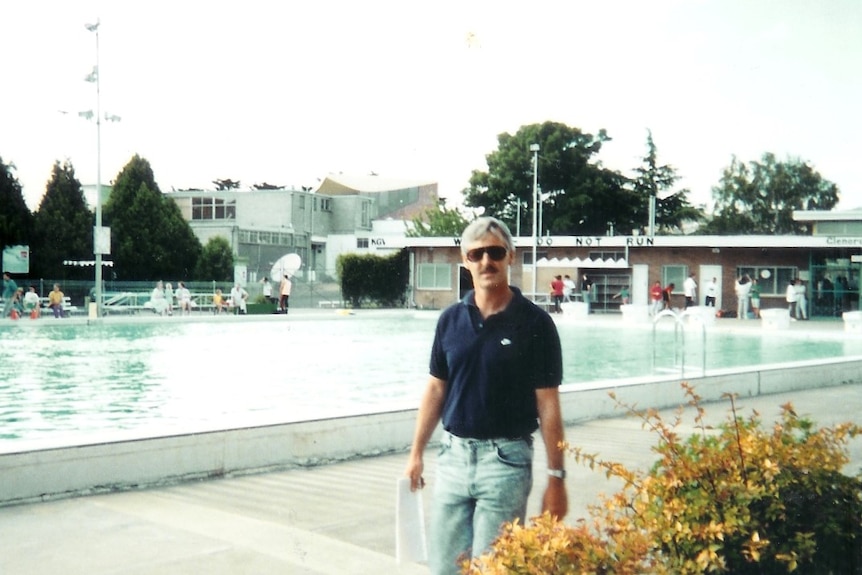 A washed out colour photograph of Chris Wedd standing with a piece of paper in his hand near the edge of the pool in 1990