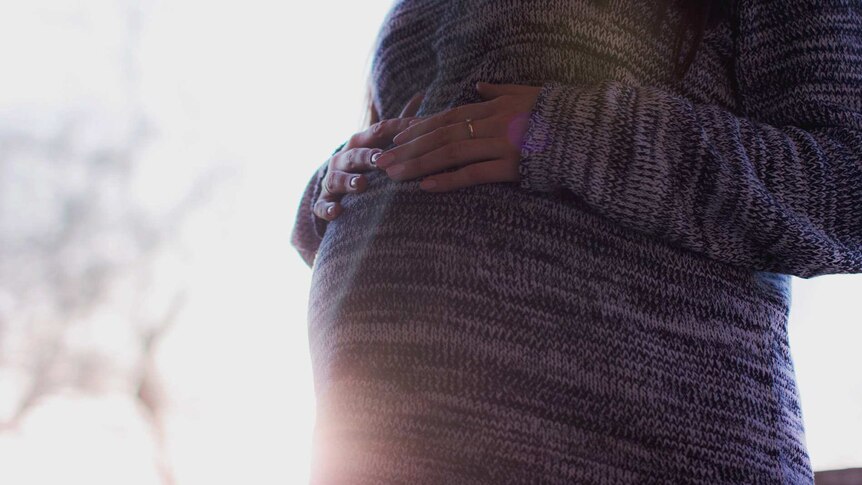 Pregnant woman wearing a jumper and holding tummy to depict what to do when you face pregnancy discrimination.