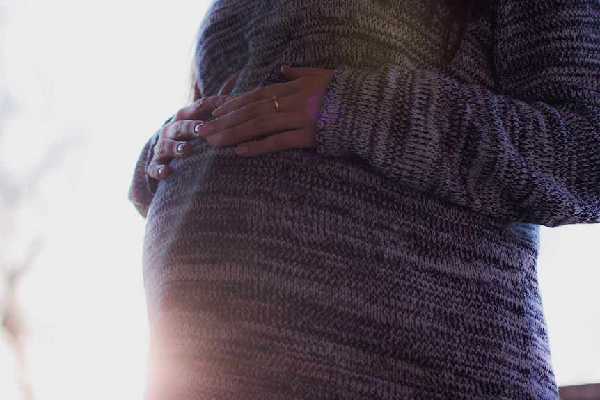 Pregnant woman wearing a jumper and holding tummy