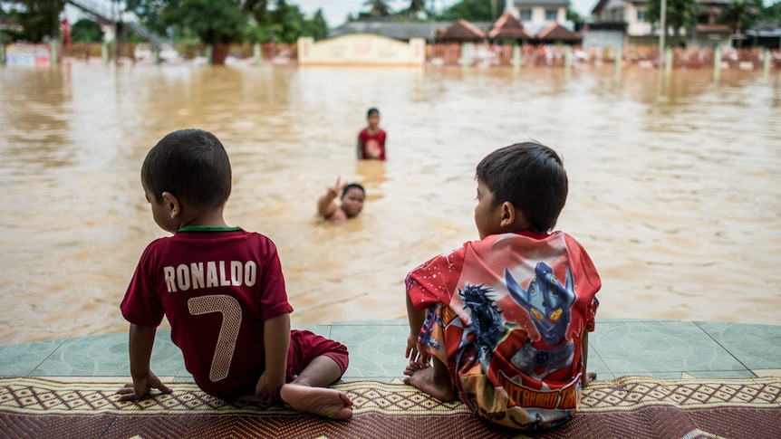 Two boys look on as their friends play in floodwaters in Pengkalan Chepa, near Kota Bharu on December 27, 2014