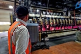 Man with a hi vis vest looks at bottles in a factory.