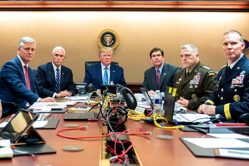 Donald Trump and five senior military and political advisers sit around a table and look forward.