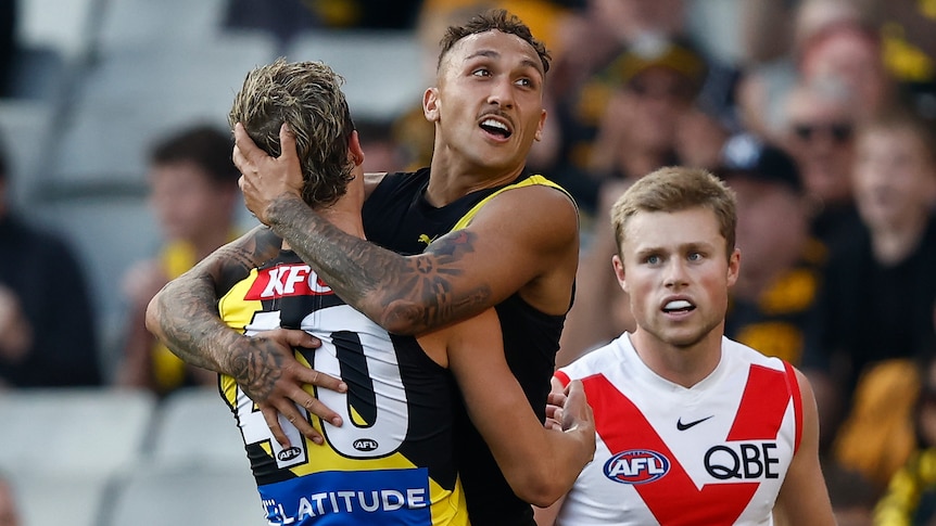 A Richmond player smiles in triumph as he hangs in the arms of a teammate after a goal in a big game.
