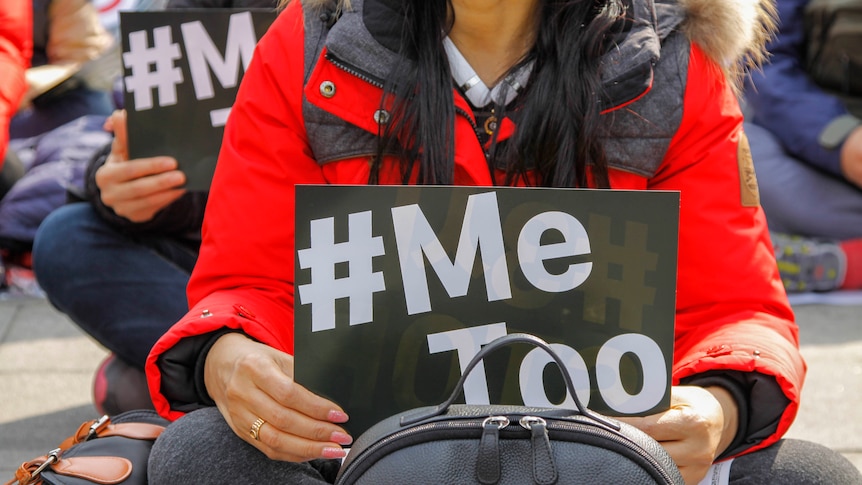 A woman holding a black-and-white sign that reads '#metoo'.