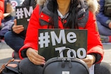 A woman holding a black-and-white sign that reads '#metoo'.