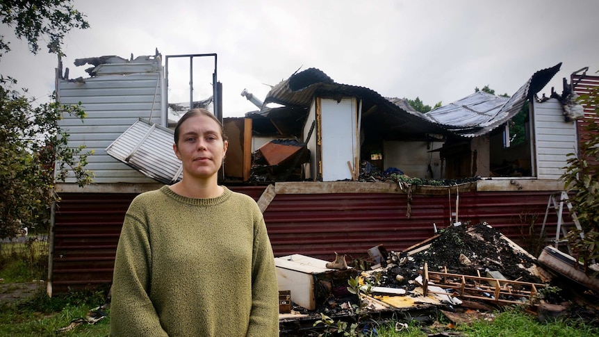 Rahima Jackson stands in front of her fire and flood-damaged house.