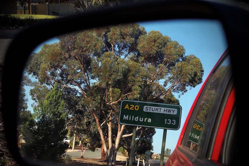 A green road sign reads Sturt Hwy, Mildura 133 kilometres. It is captured in a car mirror.