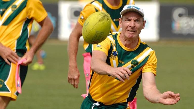 A man in a yellow shirt and white hat passes a yellow rugby ball