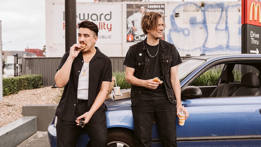 David Novak and John-Henry Pajak leaning against a car eating McDonalds