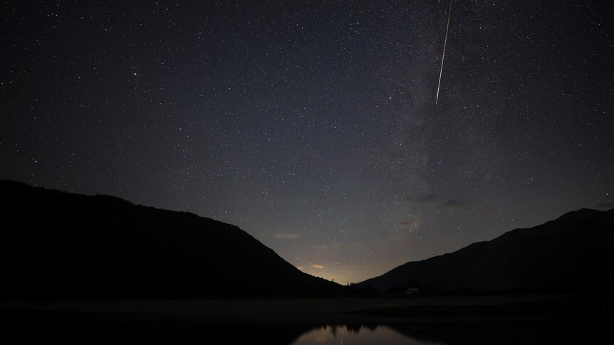 A meteor with a long white tail in the night sky.
