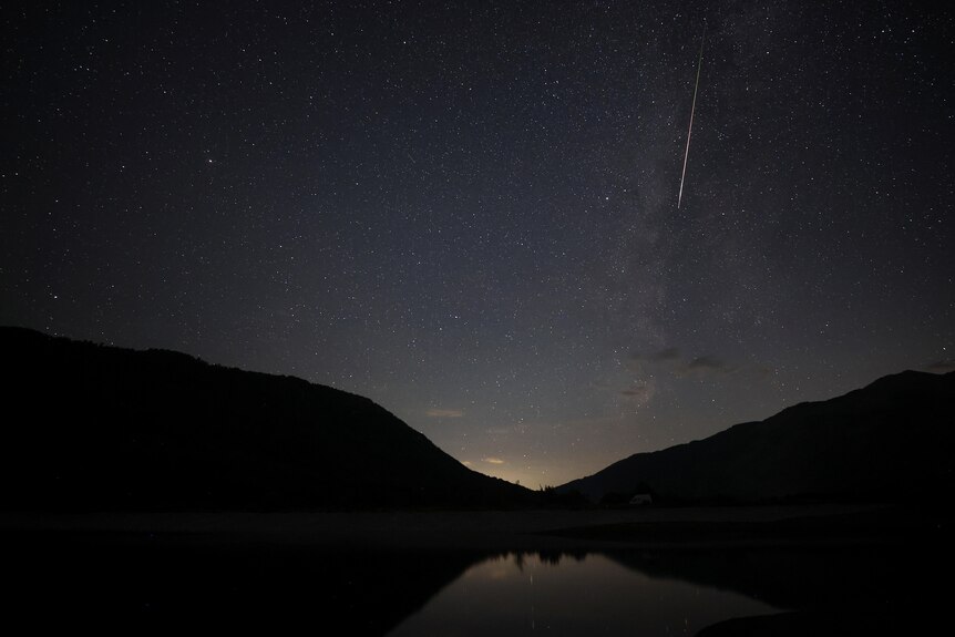 A meteor with a long white tail in the night sky.