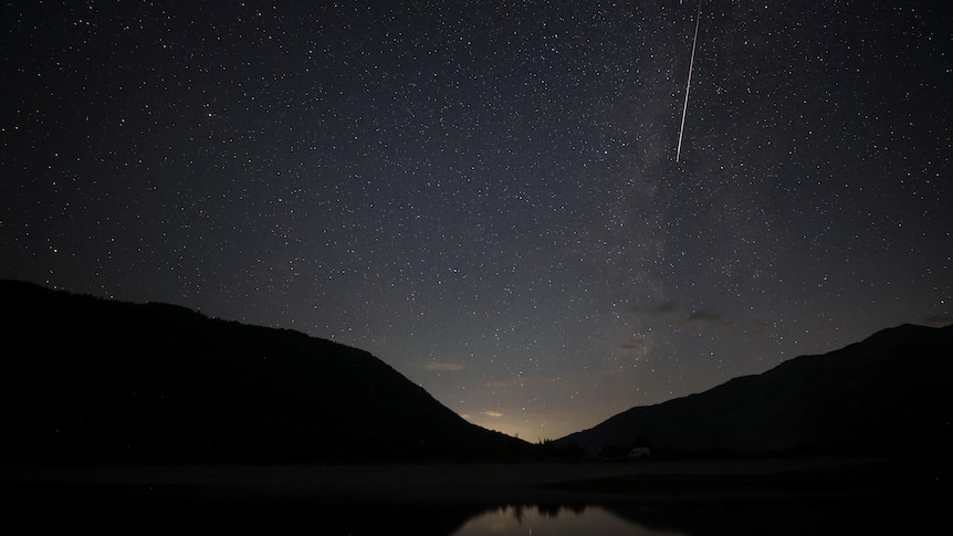 A meteor with a long white tail in the night sky.