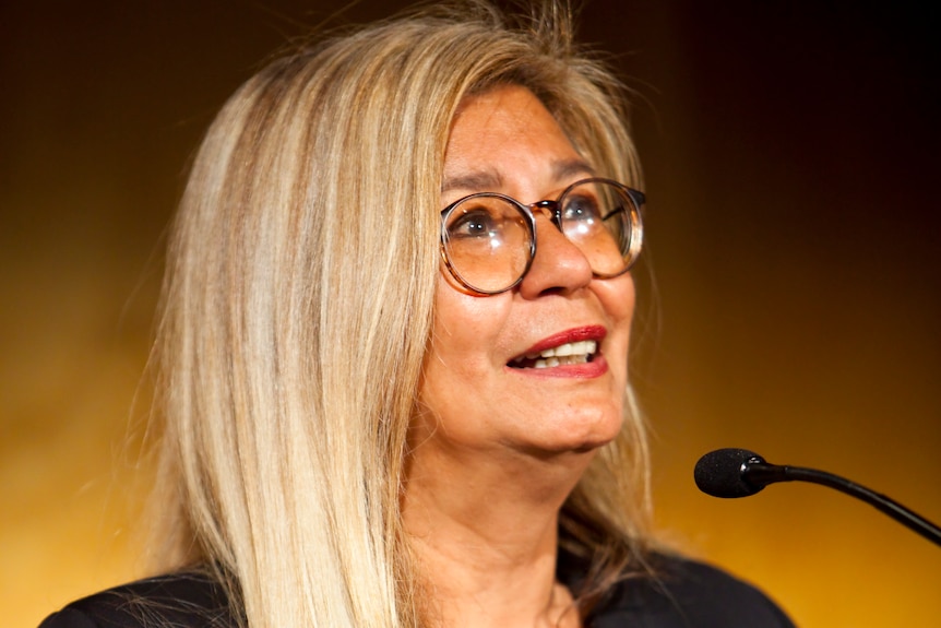 A woman speaks into a lectern microphone.