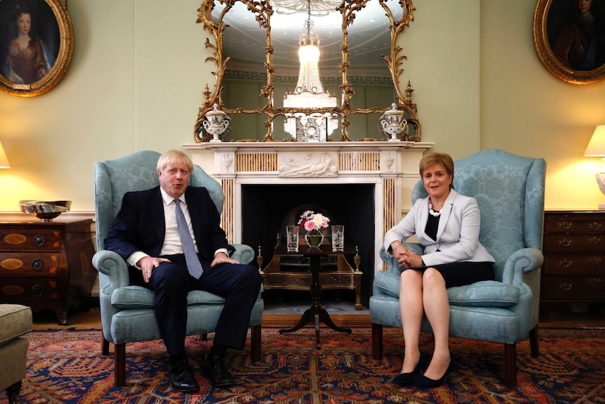 Boris Johnson sits beside Nicola Sturgeon at Bute House, Edinburgh. They are sitting on two blue armchairs.