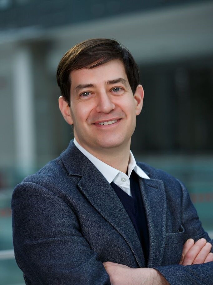 A man in a suit with folded arms smiles at the camera.