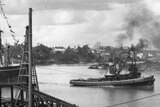Black and white photo of steam-powered tug boat towing steam ship triple its size in river