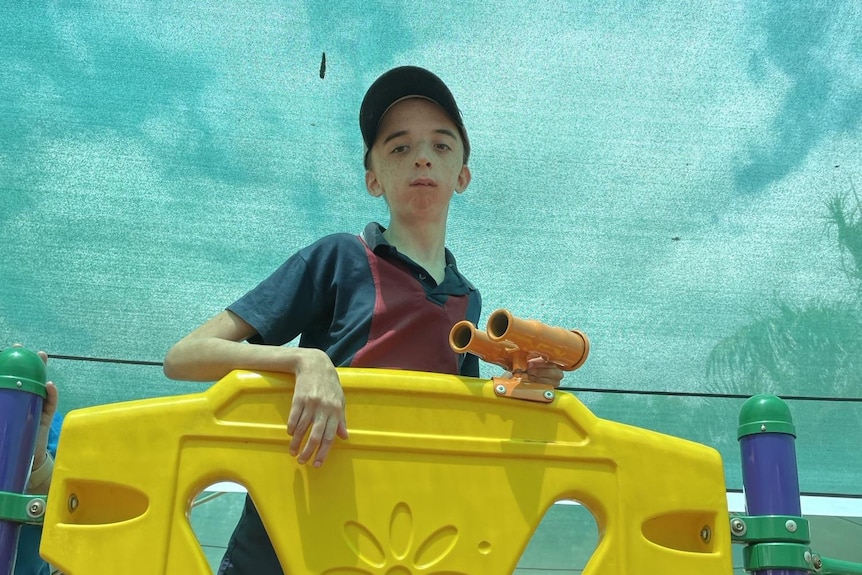 A yong man standing on a yellow playground set. 