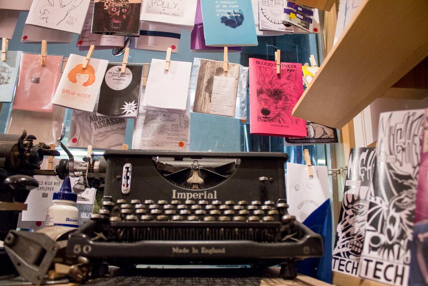 An old typewriter, photocopied and printed magazines and comics hang from pegs.