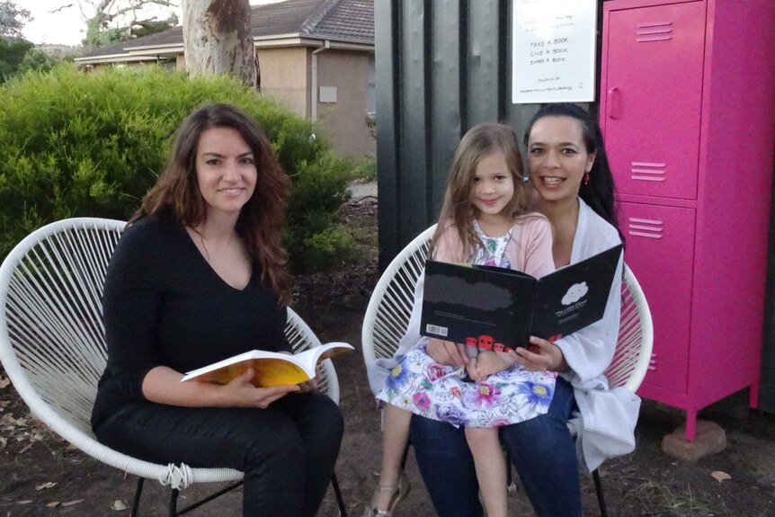 Two women and a young girl sit at a street library.