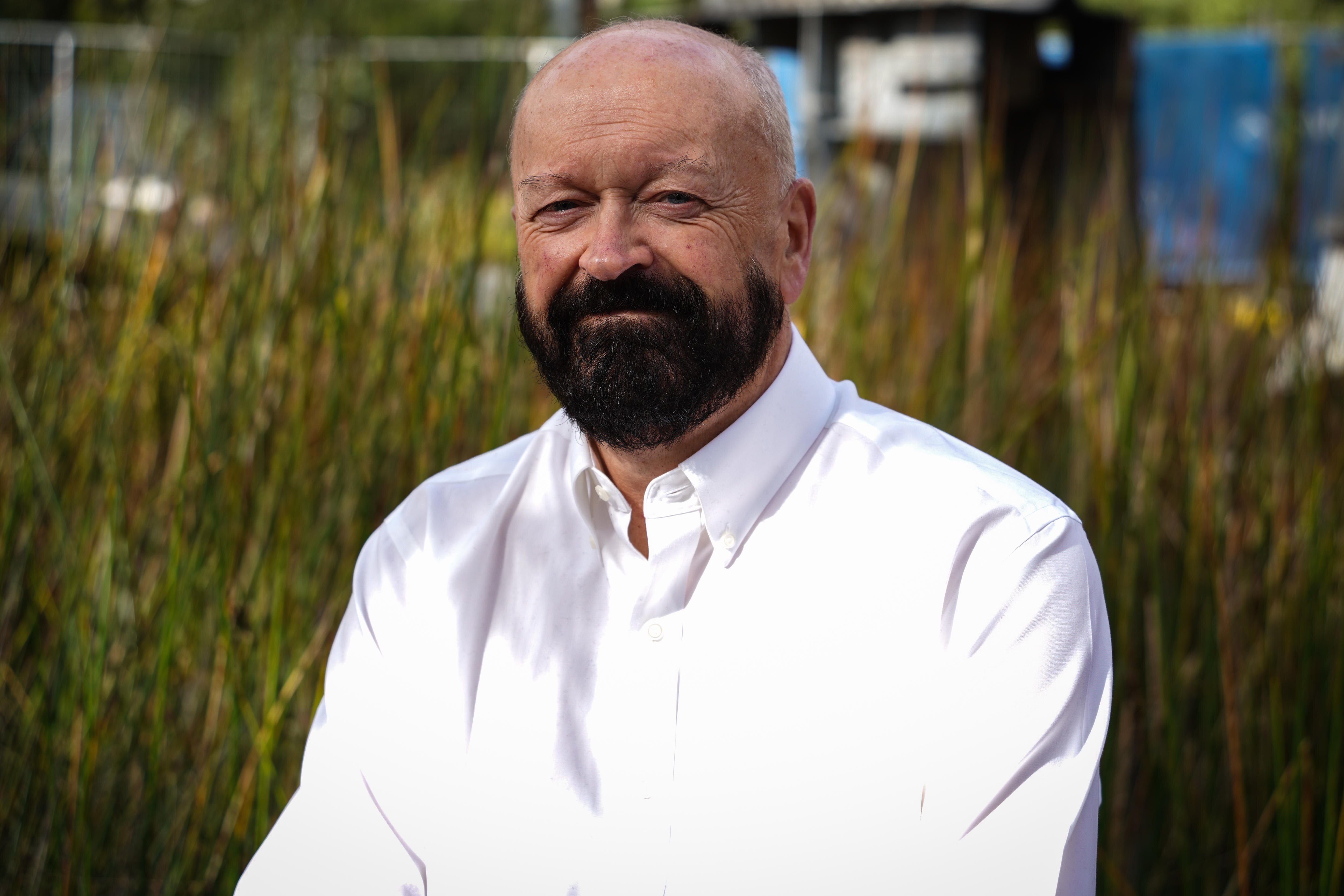 A man with a black beard and wearing a white shirt sits for a portrait.
