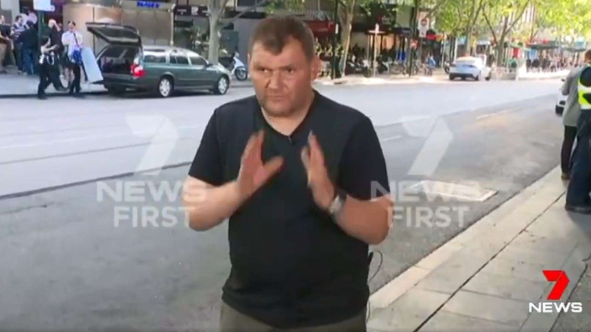 A man raises his hands, recreating pushing a trolley.