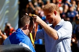 Harry wearing a blue shirt placing a medal around the neck of a man