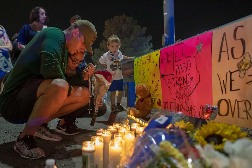 A men bends over in front of signs, candles and toys for victims