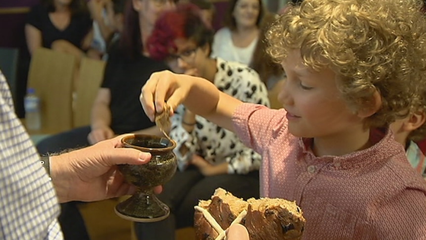 A boy dips hot cross bun into wine