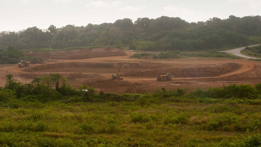 A wide shot of heavy machinery and trucks at the Phosphate Hill mine site, surrounded by green trees.