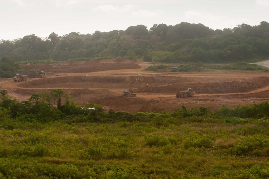 A wide shot of heavy machinery and trucks at the Phosphate Hill mine site, surrounded by green trees.