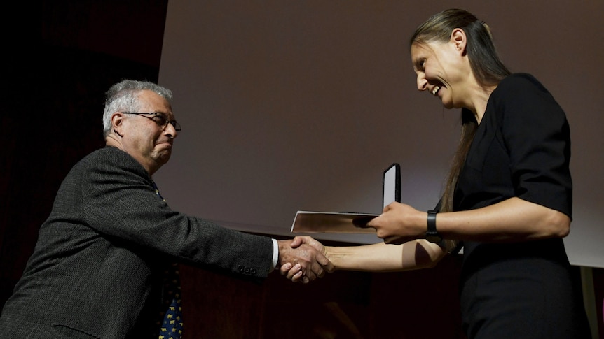 A woman holds an award while she shakes hands with a man