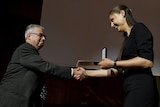 A woman holds an award while she shakes hands with a man
