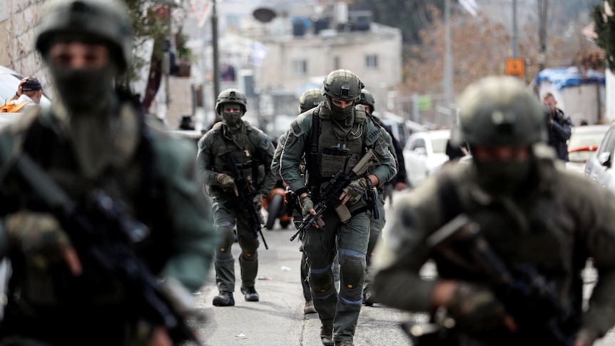 Army forces are pictured walking through a street, heavily armed.