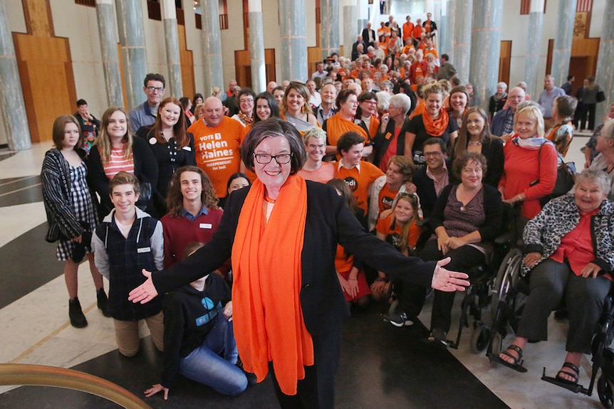 L'indépendante Cathy McGowan (avec un foulard orange) se tient devant un groupe de personnes les bras ouverts.