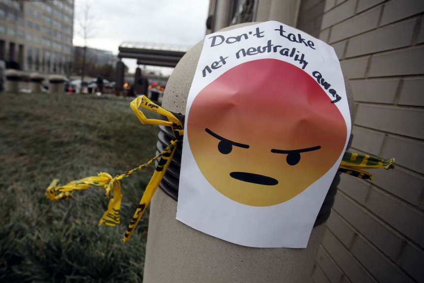 A sign with an emoji reads "Don't take net neutrality away" is posted on a bollard.