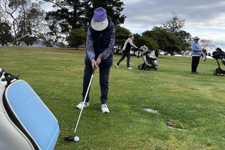 An elderly lady lines herself up to tee off on a golf green 