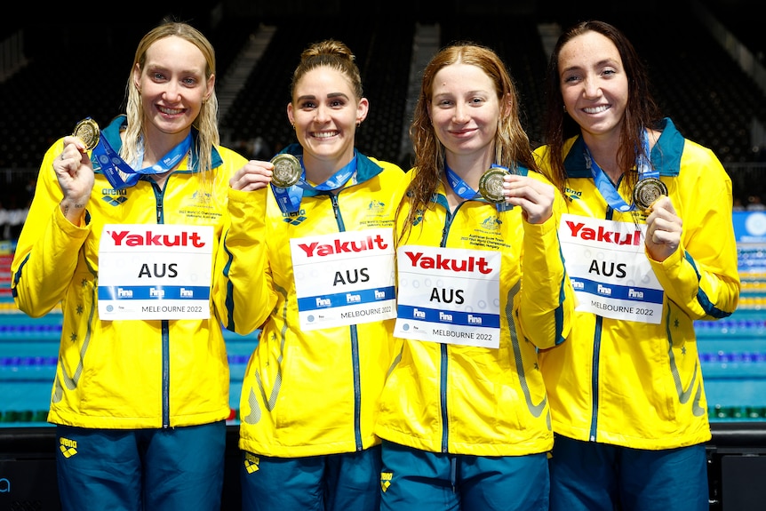Four women in yellow smile and hold up gold medals