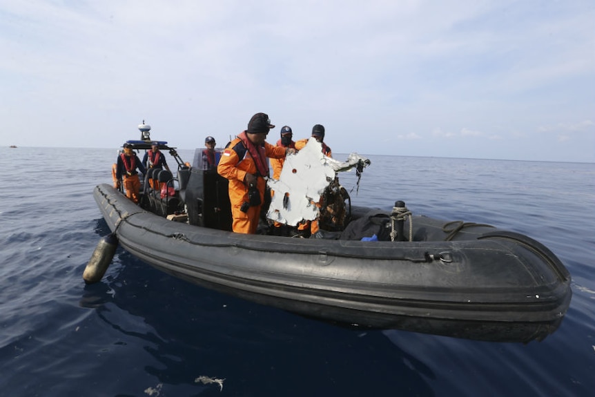 Rescuers examine wreckage as they search waters in an inflatable boat