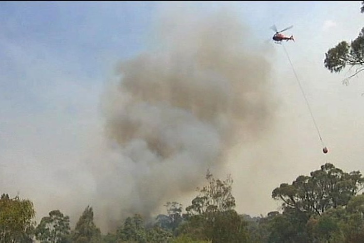 A water bombing helicopter flies past a bushfire smoke plume. good generic