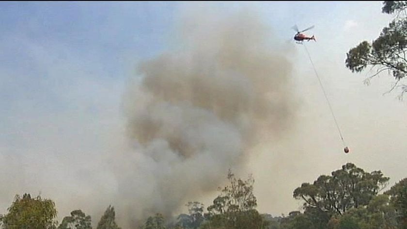 A water bombing helicopter flies past a bushfire smoke plume