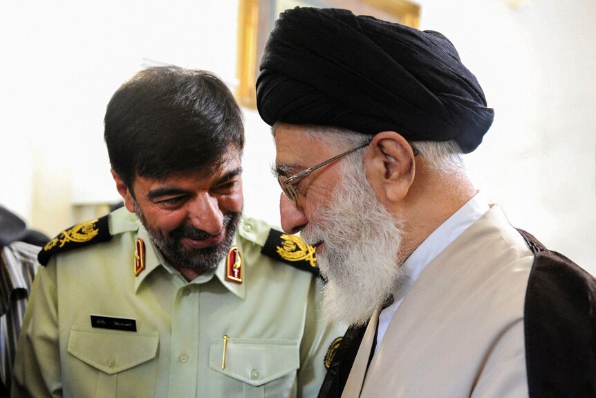 Iran's Supreme Leader Ayatollah Ali Khamenei smiles and talks to Ahmad-Reza Radan, who is wearing a uniform.