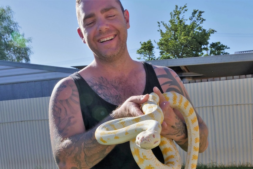 A man smiling with a white and yellow snake.