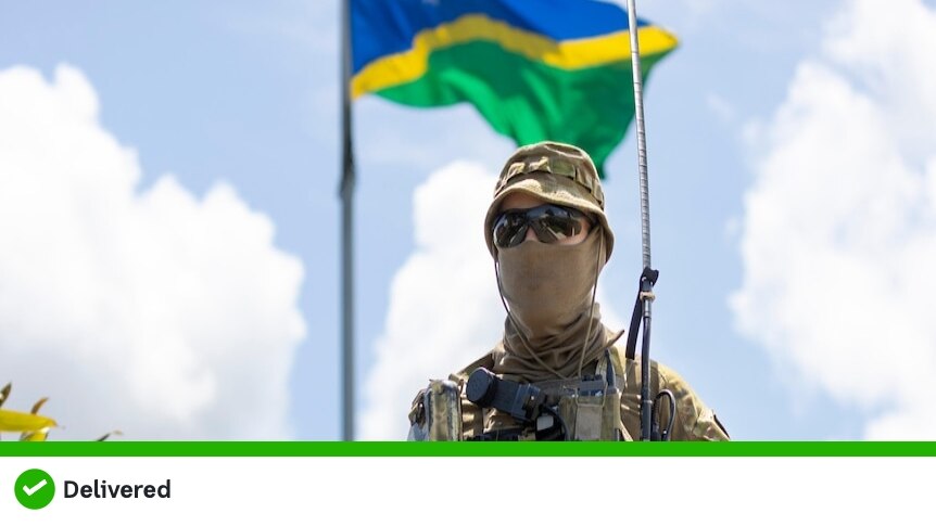 A soldier stands in front of the flag of Solomon Islands out of focus in the background