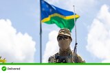 A soldier stands in front of the flag of Solomon Islands out of focus in the background