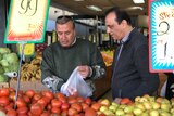 Tony Fares selects tomatoes at a fruit shop with a friend